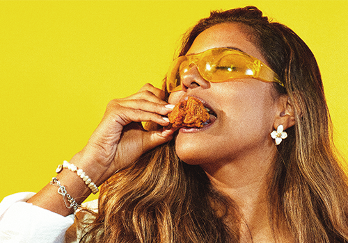 Mulher com óculos amarelos comendo frango frito