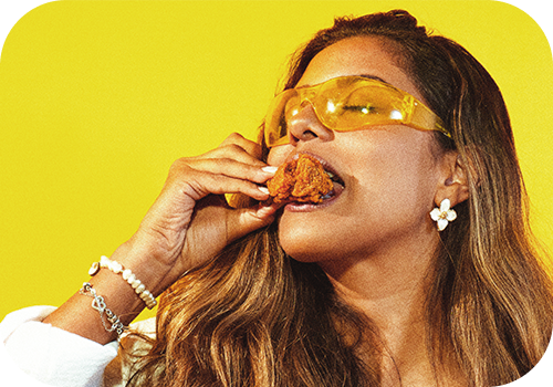 Mulher com óculos amarelos comendo frango frito